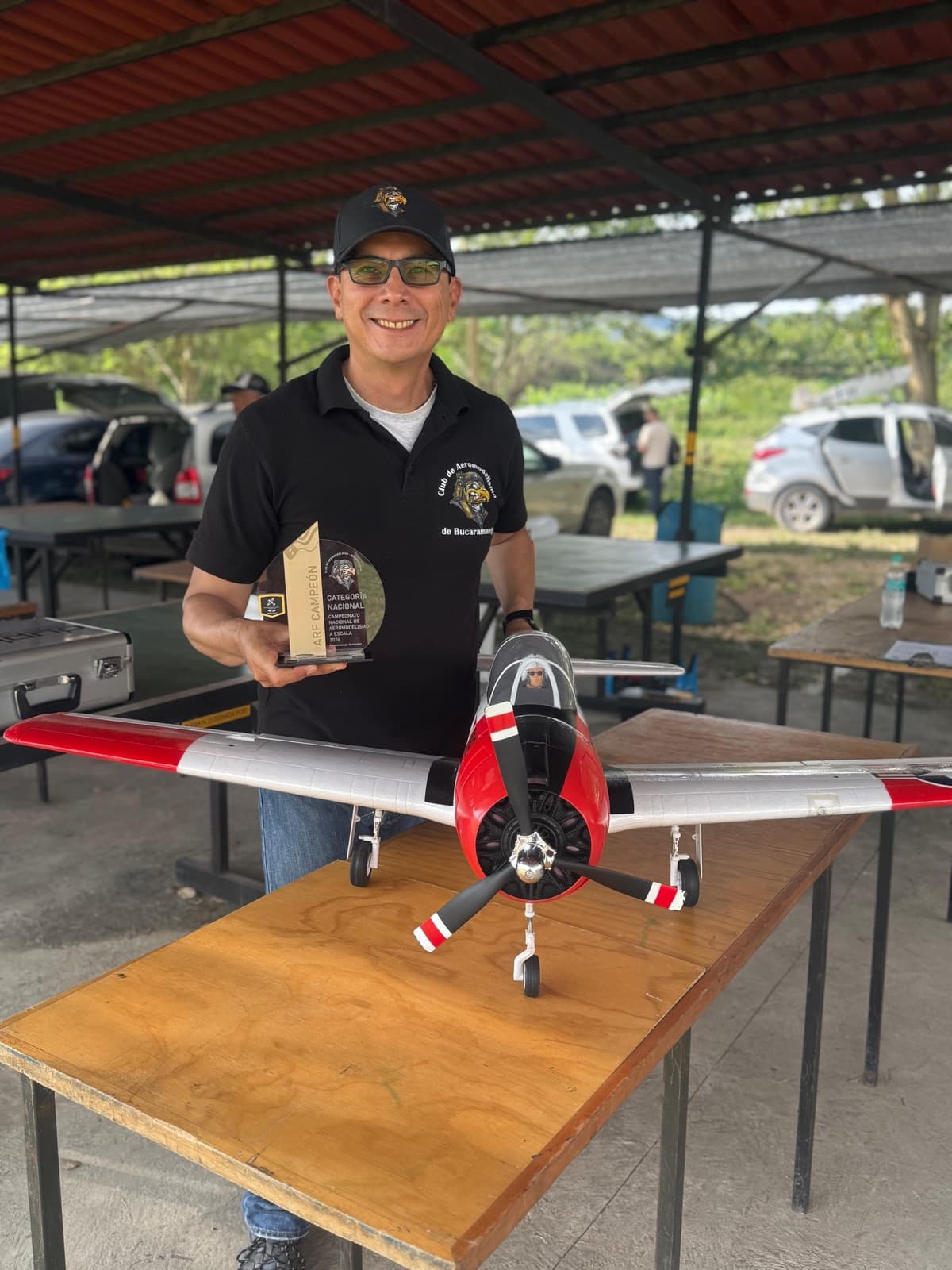 Germán Melo sostiene un trofeo junto a su avión rojo y blanco de hélice tripala, apoyado sobre una mesa en los pits.